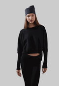 ARMERS Pullover in black with drop sleeves and high-low bodice, modeled by woman in black leggings.