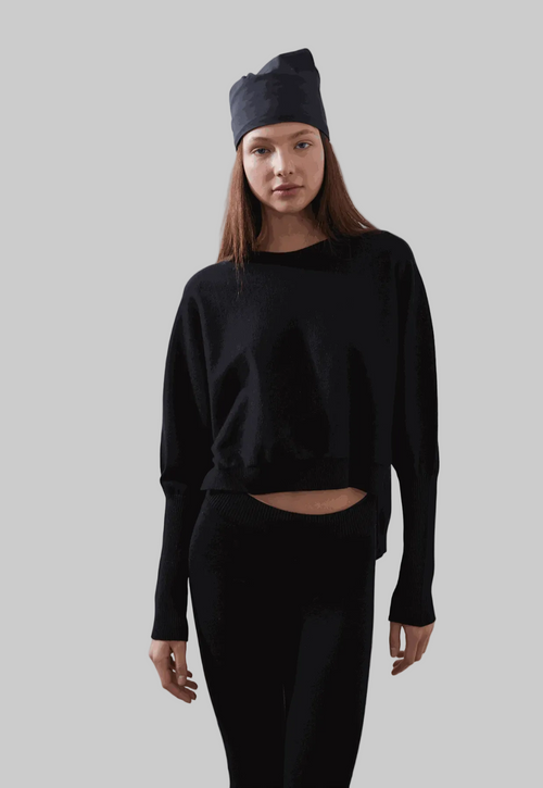 ARMERS Pullover in black with drop sleeves and high-low bodice, modeled by woman in black leggings.